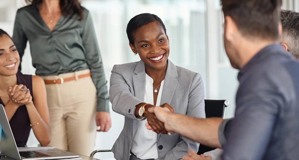 A woman shaking hands with another person in front of other people.