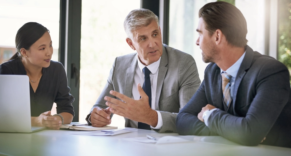 Three men in suits sitting at a table talking.