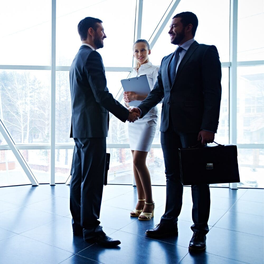 Two businessmen shaking hands, colleague holding clipboard